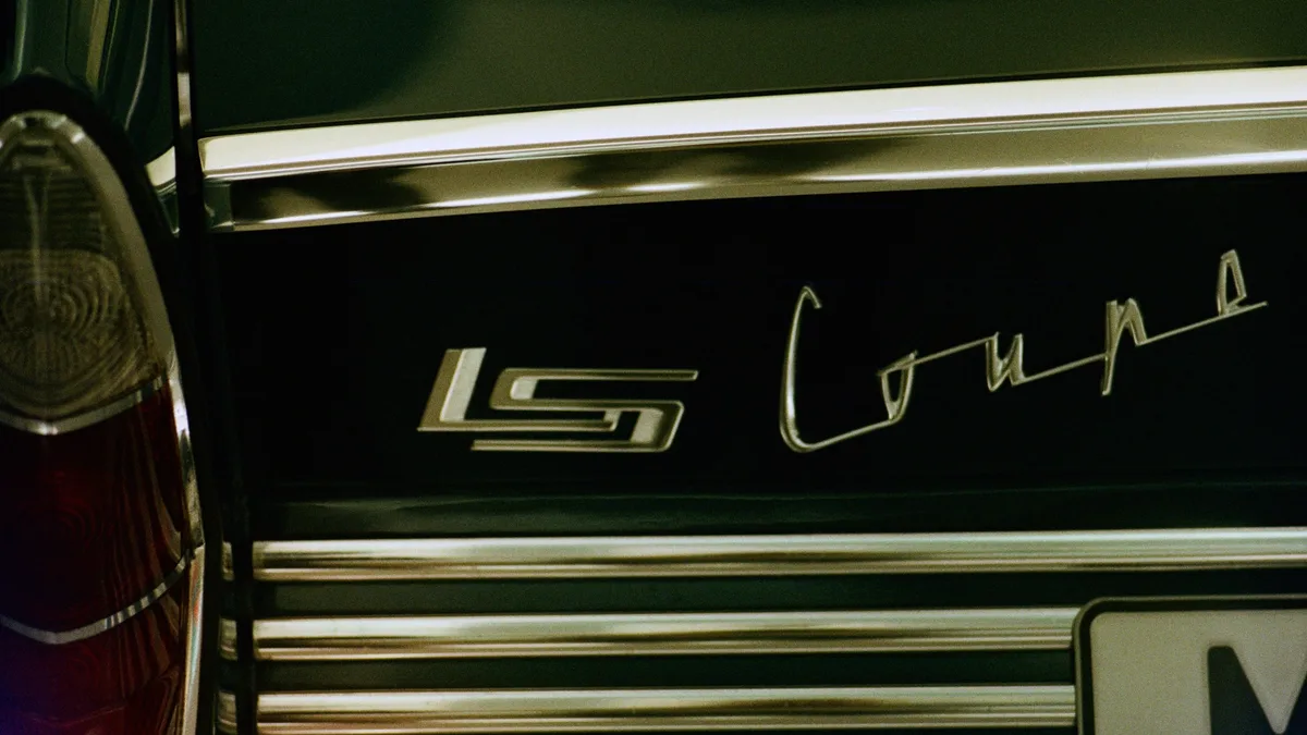 The rear of a vintage car with a black body and chrome trim, featuring the "LS Coupe" logo in gold lettering.