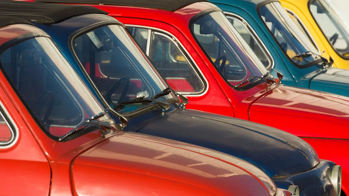 The front ends of four vintage cars, each with a distinctive color scheme and windshield design.